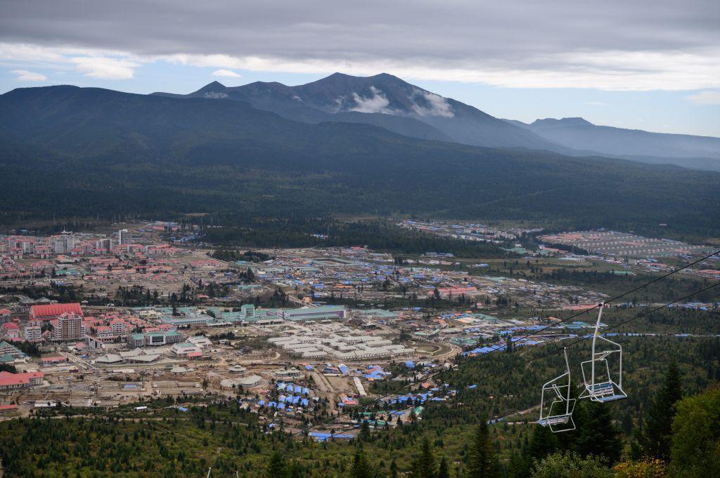 A distant view of the city of Samjiyon, with a chairlift in the foreground and mountains in the background.