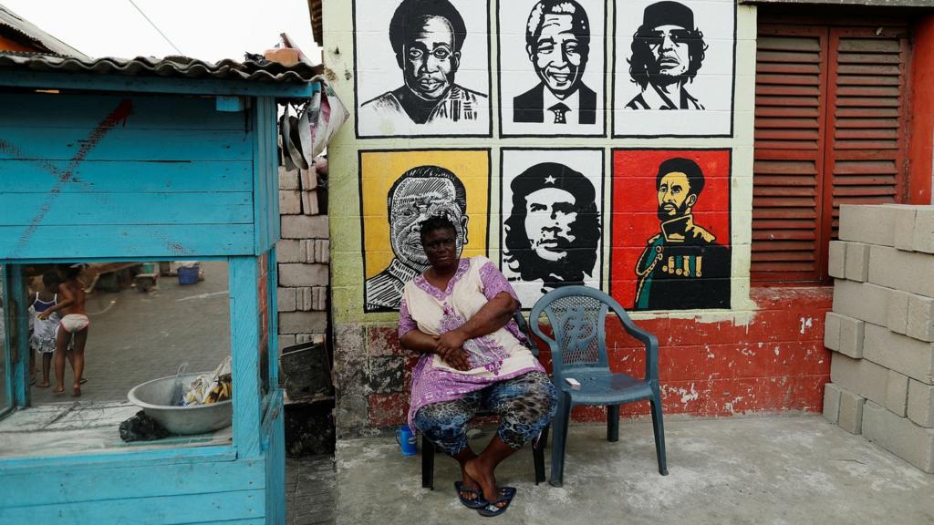 A vendor sits next to a mural depicting African leaders in Ghana's capital, Accra.