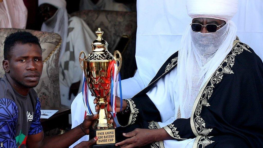 A Dambe fighter from the House of Arewa accepts the Emir Ado Bayero Dambe Championship trophy from His Highness the Emir Aminu Ado Bayero