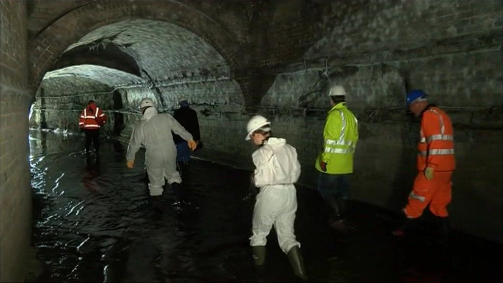 Workers wearing high vis jackets and hard hats, walking through a dark tunnel where the River Sherbourne lies