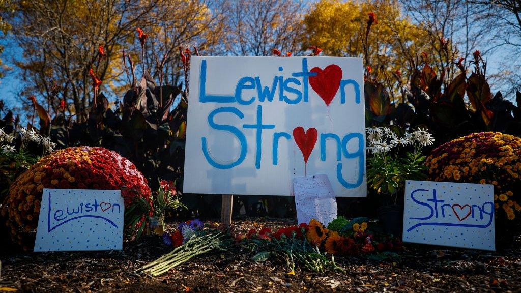 A sign indicating Lewiston's strength, along with bouquets of flowers, is seen in downtown Lewiston