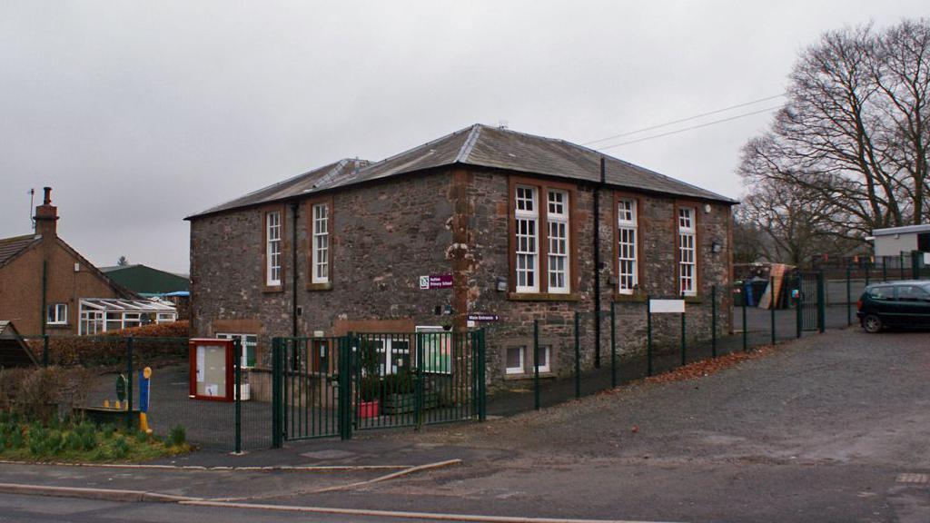 An old school building in southern Scotland on a grey day with large windows and a sprawling tree behind it