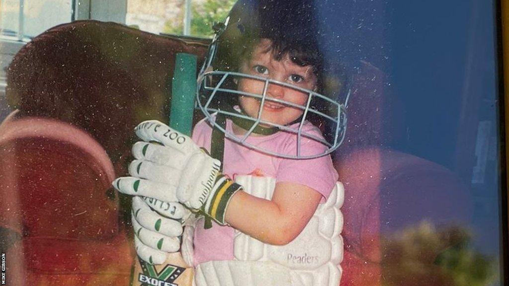 Danielle Gibson as a child with a full size bat, pads and helmet