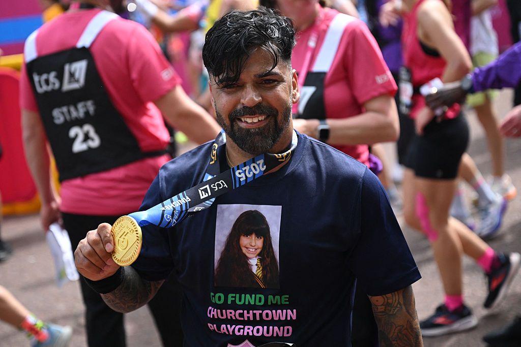 Sergio Aguiar, wearing a shirt displaying a picture of his daughter, Alice, and text reading Go Fund Me Churchtown Playground poses with his medal as he finishes the 2025 London Marathon