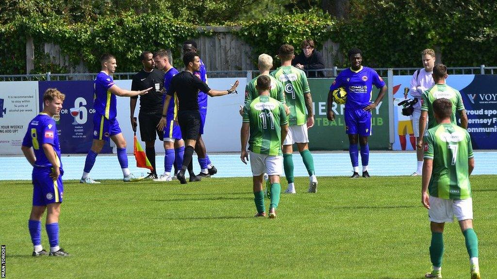 Players surround the referee during the red card incident at Guernsey FC