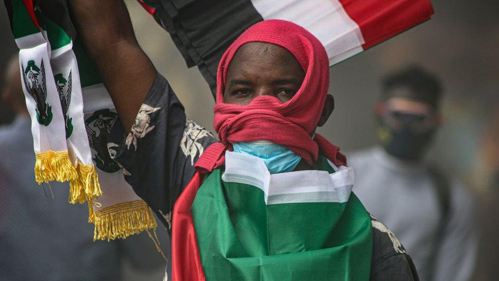 A man with a flag draped around his back holds his arm in the air