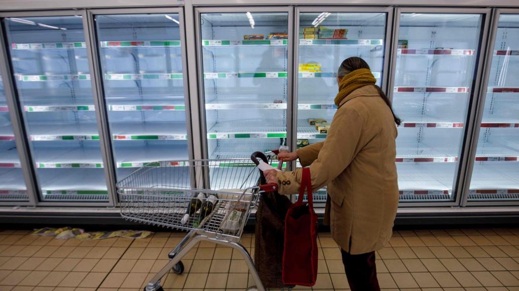 People shop in aisles with empty shelves in a Sainsbury's supermarket in Walthamstow