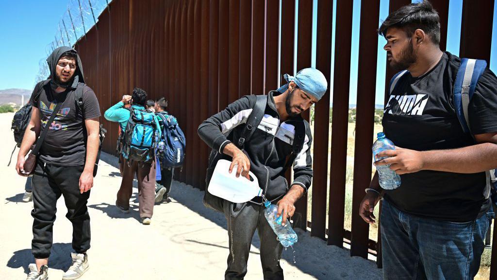 Migrants from India's Punjab region pause for water while walking beside the US-Mexico border wall at at Jacumba Hot Springs, California on June 5, 2024.