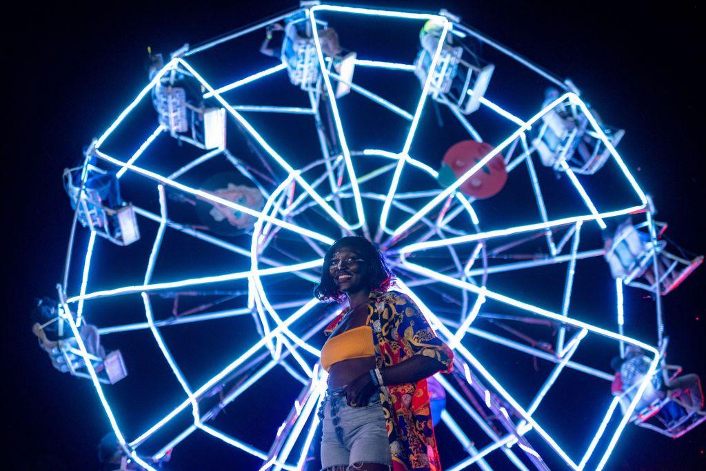 A woman stands in front of a ferris wheel that is brightly lit up at the Nyege Nyege festival in Uganda - Saturday 16 November 2024