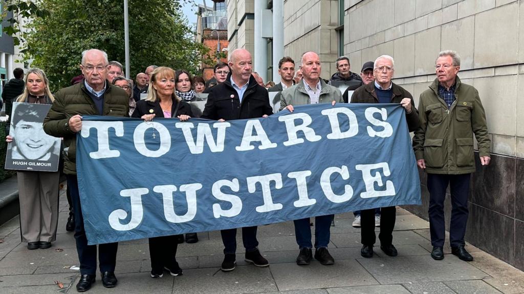 A crowd of people holding a banner which says 'Towards Justice' walking 