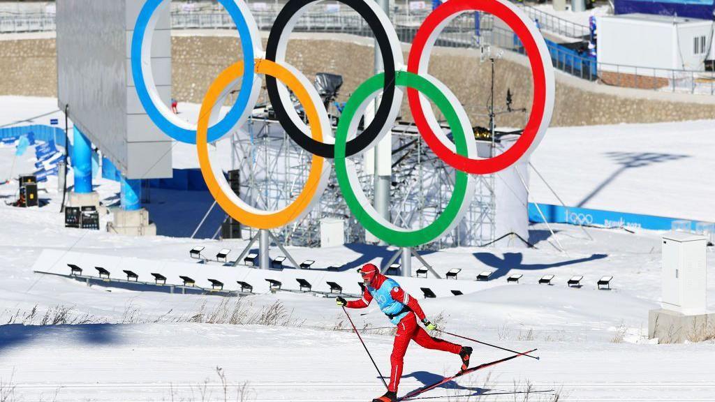 A cross-country skier in front of the Olympic rings
