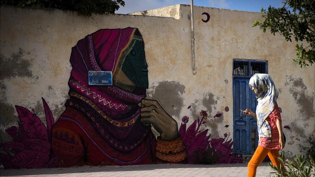 A woman walks past a mural by Mexican artist SANER in the village of Erriadh, on the Tunisian island of Djerba, on August 7, 2014, as part of the artistic project 'Djerbahood'.