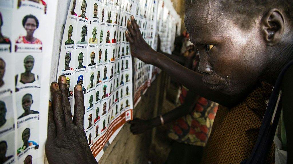 A woman looking at wall of pictures to identify missing loved ones