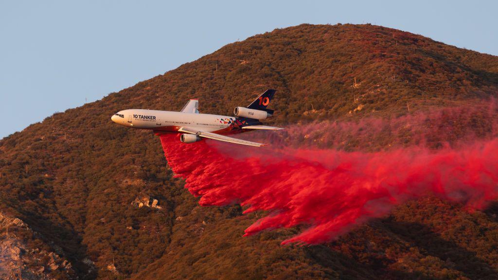 A plane flies near a hill, depositing pink dust as it goes