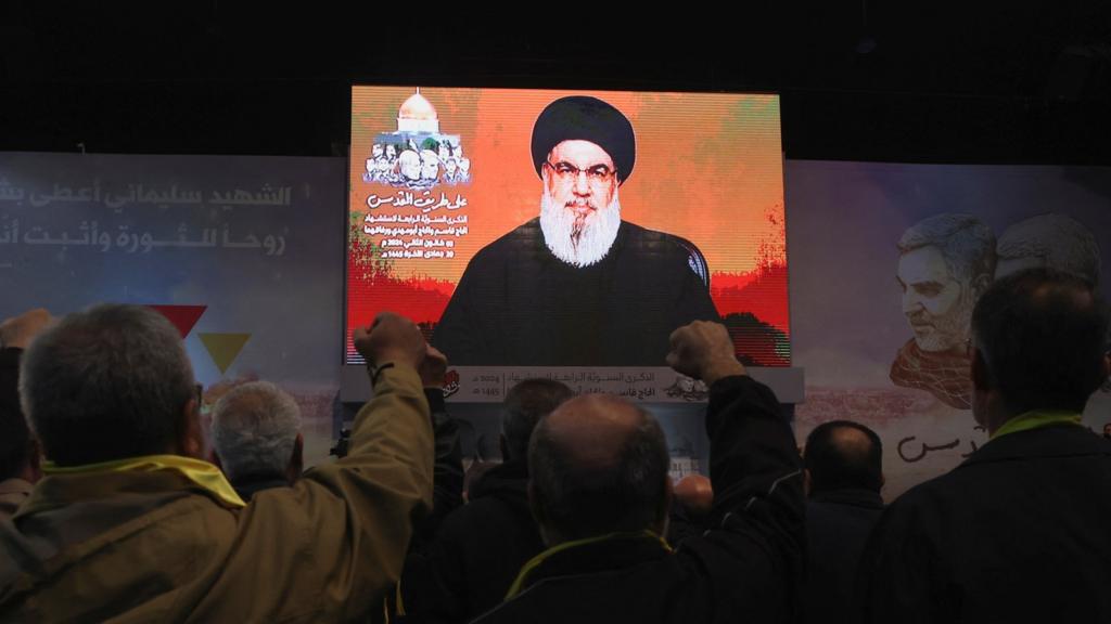 Hezbollah leader Hassan Nasrallah giving a speech on a projector screen in front of an audience