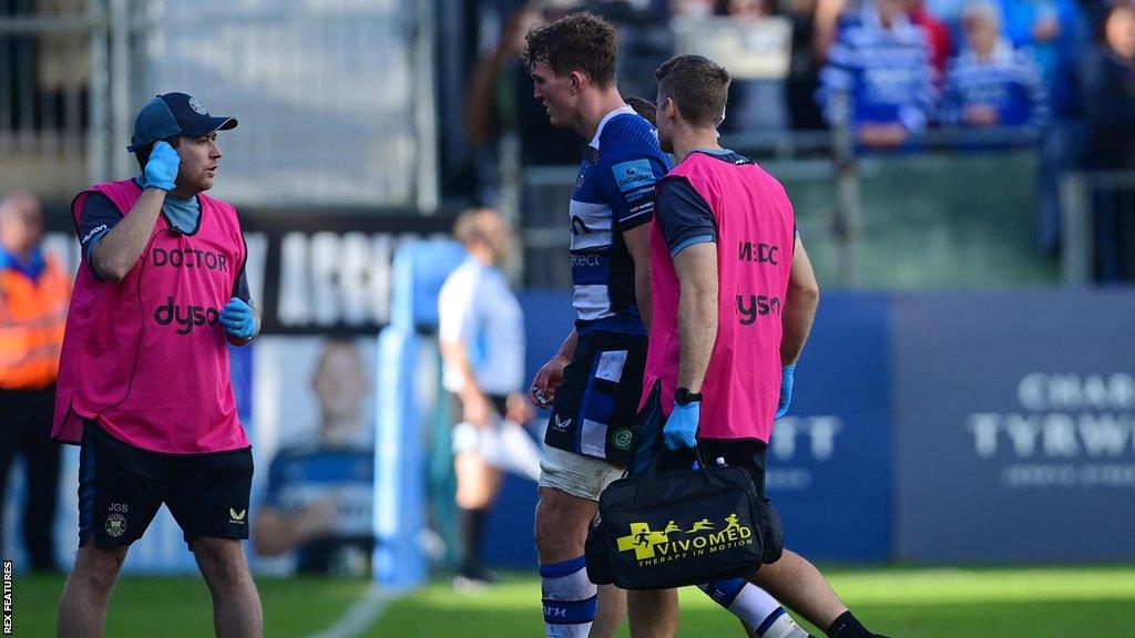 Ted Hill walks off the pitch alongside medical staff