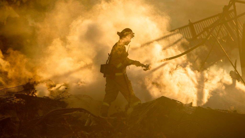 A firefighter sprays down the smouldering remains of a home during the Hillside Fire in the North Park near San Bernardino, California