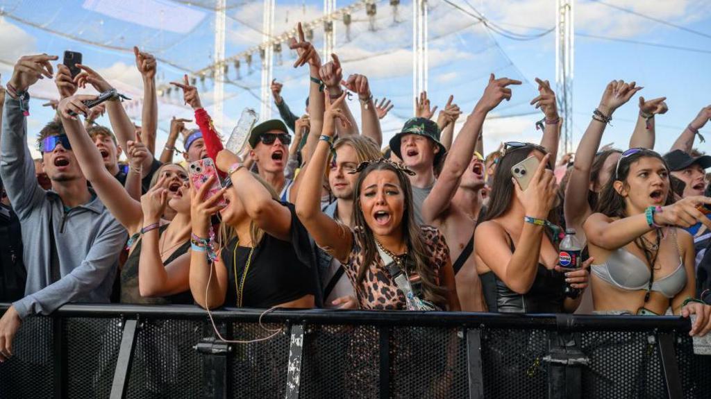 Festival goers dancing with their hands in the air next to a barrier at Leeds Festival in 2024.