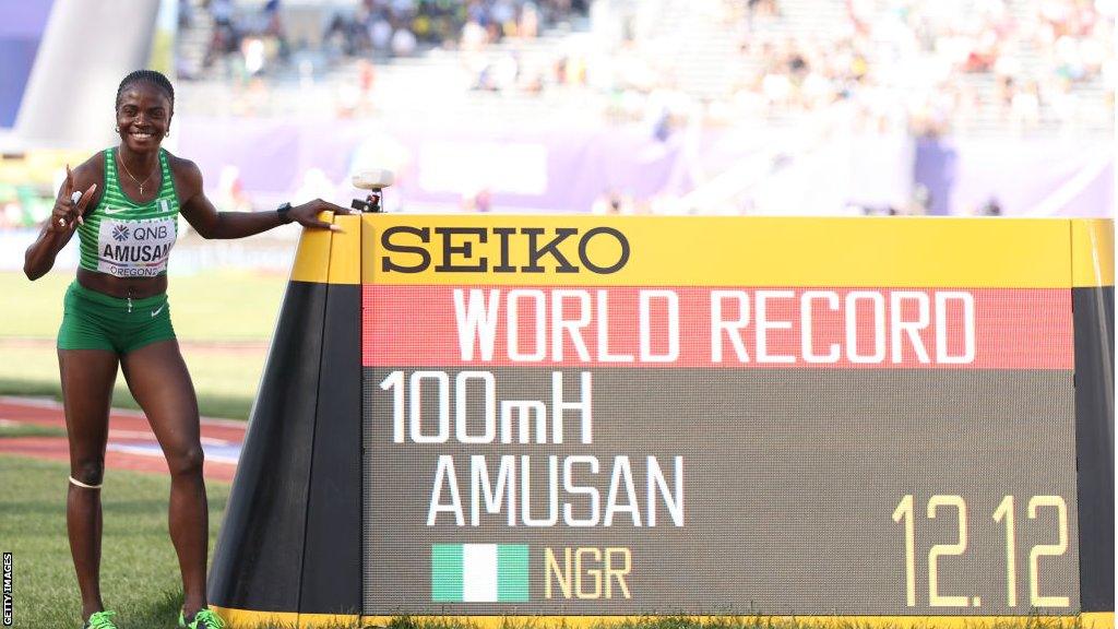 Tobi Amusan stands next to a screen with confirmation of her world record time for 100m hurdles