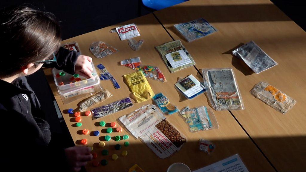 Person sitting at table covered in plastic waste.