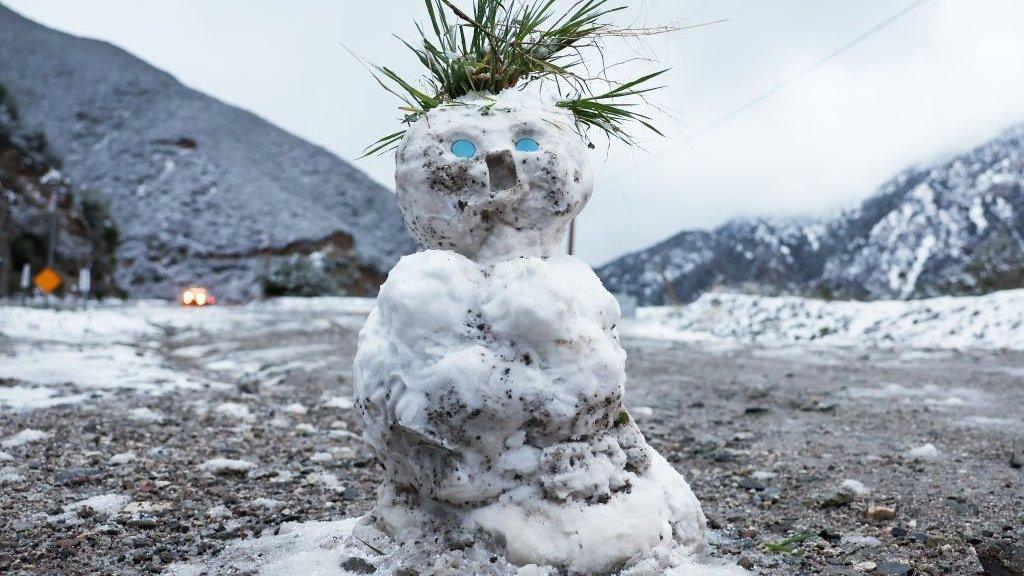 A snowman stands against a background of California mountains