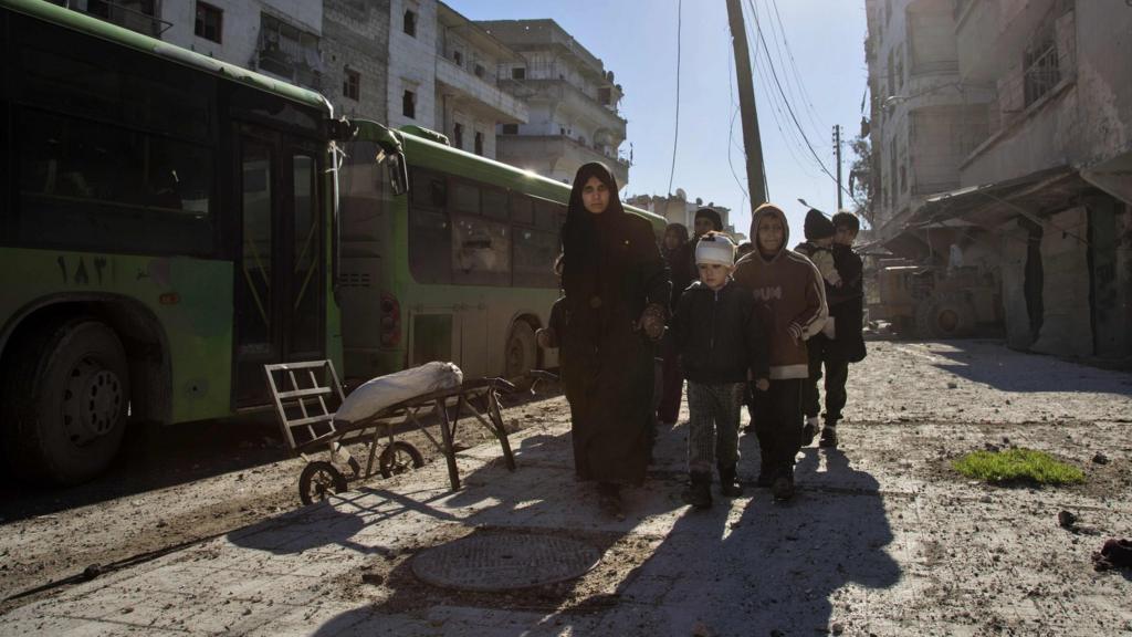 Injured boy and family walk next to evacuation bus