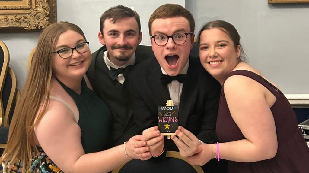 A group of people wearing formal dress and holding an award reading "best writing".