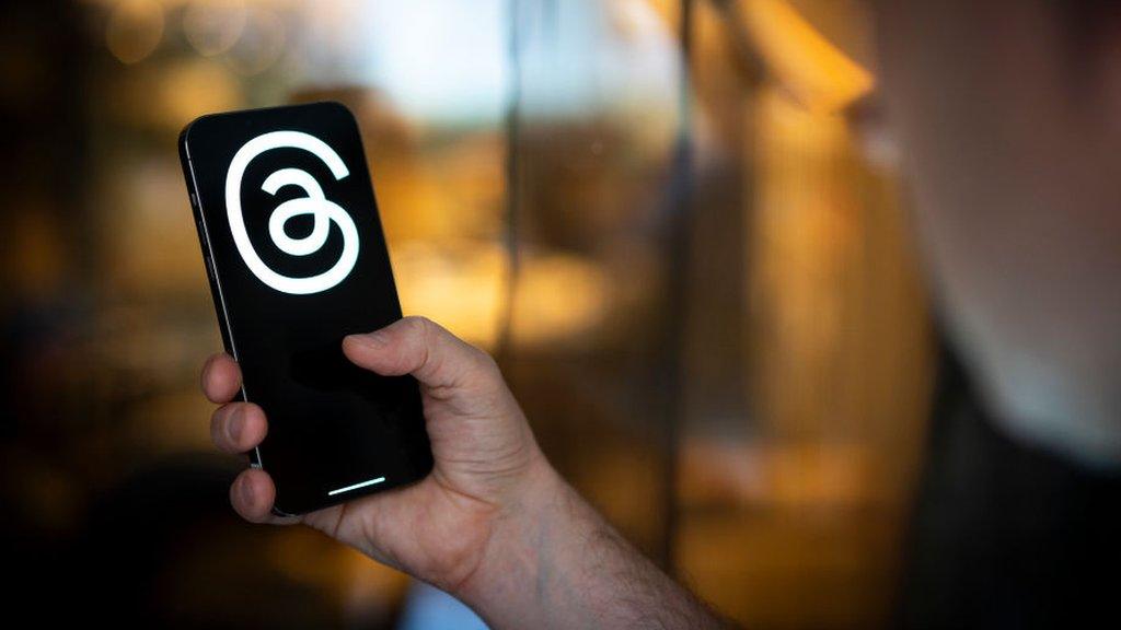 A stock photo of someone holding a phone with the Threads logo on screen