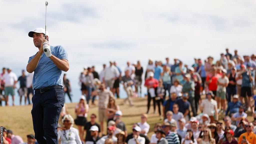 Scottie Sheffler watches a shot with fans gathered on the hill behind him