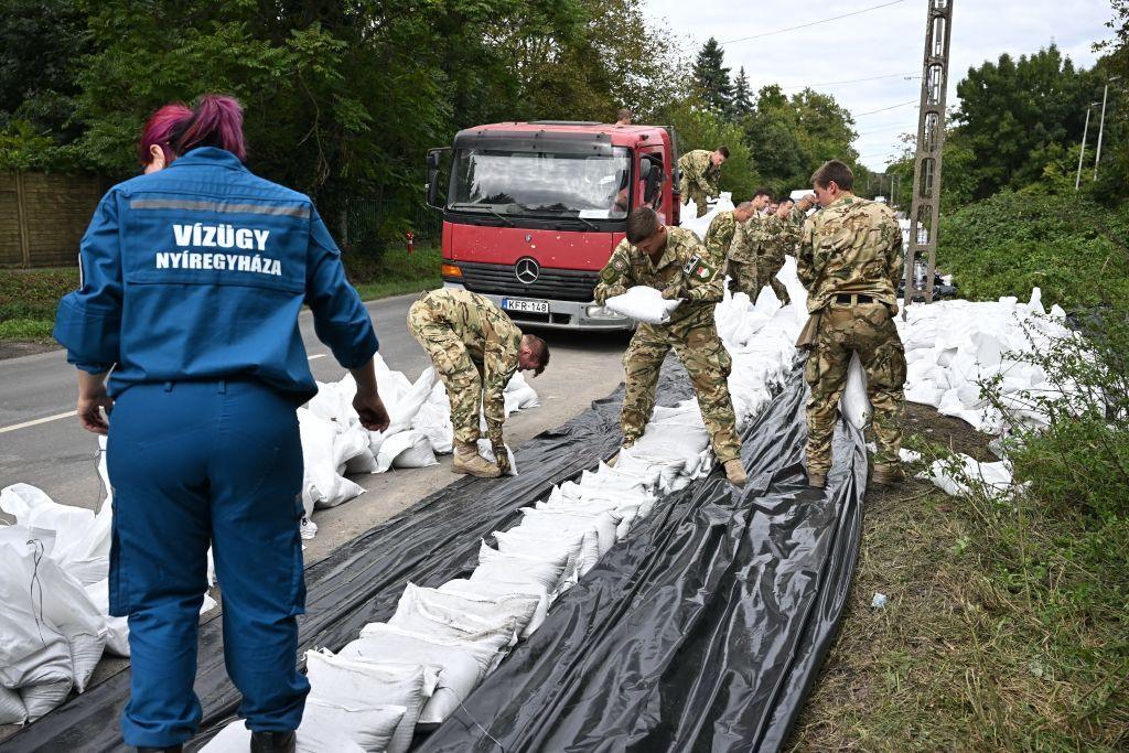 More than a dozens soldiers in uniform are piling up sand bags and plastic sheets as a temporary flood barrier 