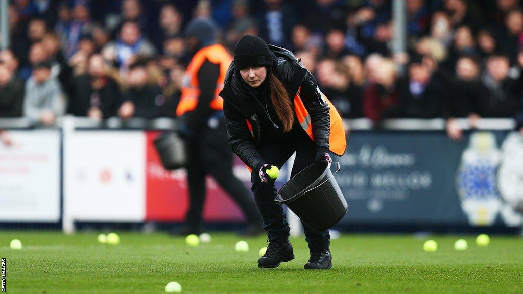 A steward collects tennis balls off the pitch during FA Cup round two fixture, Eastleigh v Reading