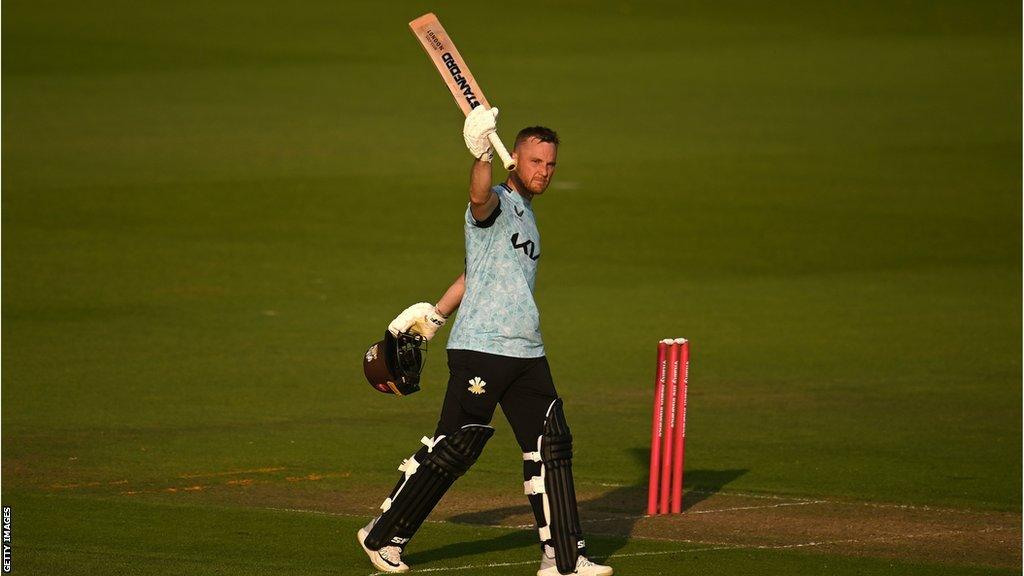 Laurie Evans raises his bat after reaching 100