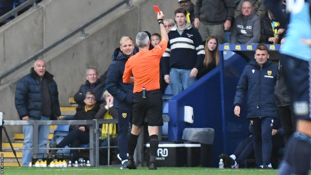 Oxford United boss Liam Manning is shown a red card.