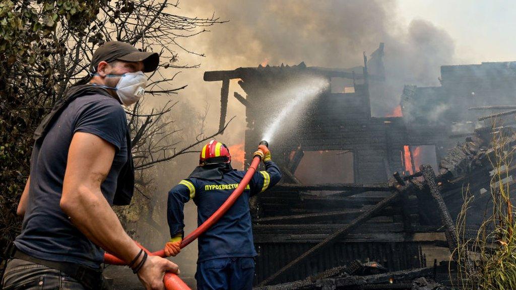 A volunteer helps firefighters put out the flames from a burning house in the Afidnes area of northern Athens on August 6 2021