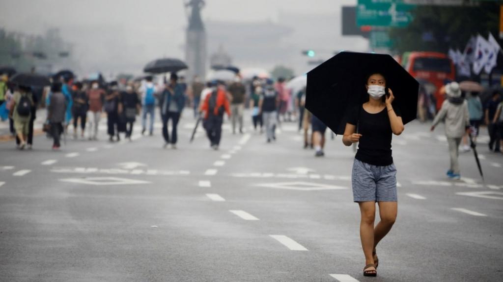 A woman wearing a mask walks past members of conservative civic groups in Seoul, South Korea