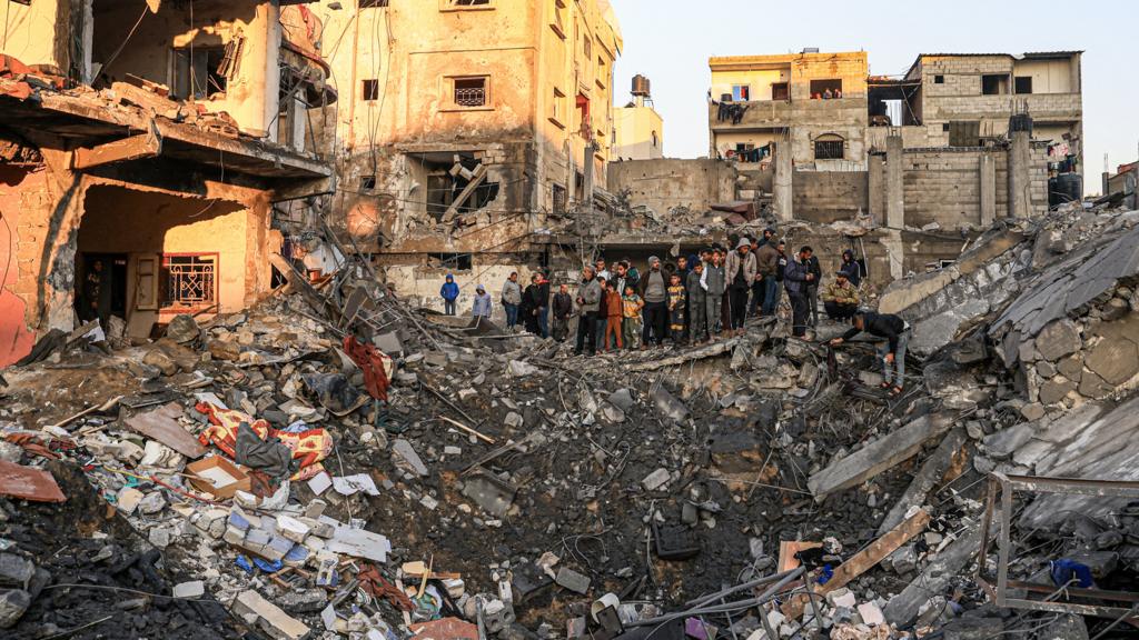 People stand on the edge of a crater caused by an Israeli bombardment as they inspect the destroyed building