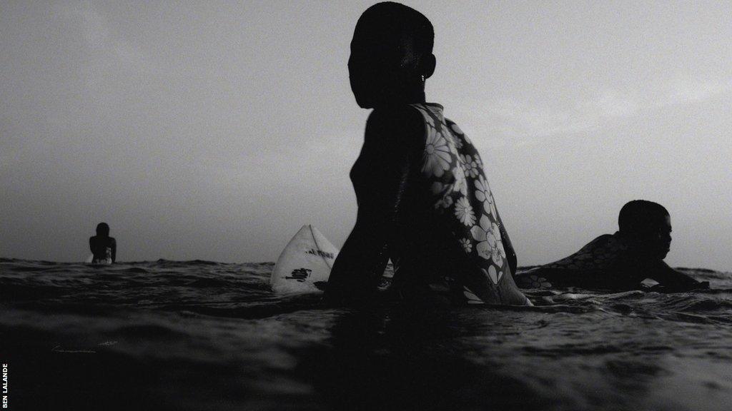 A surfer sits on her board in silhouette in a black and white image