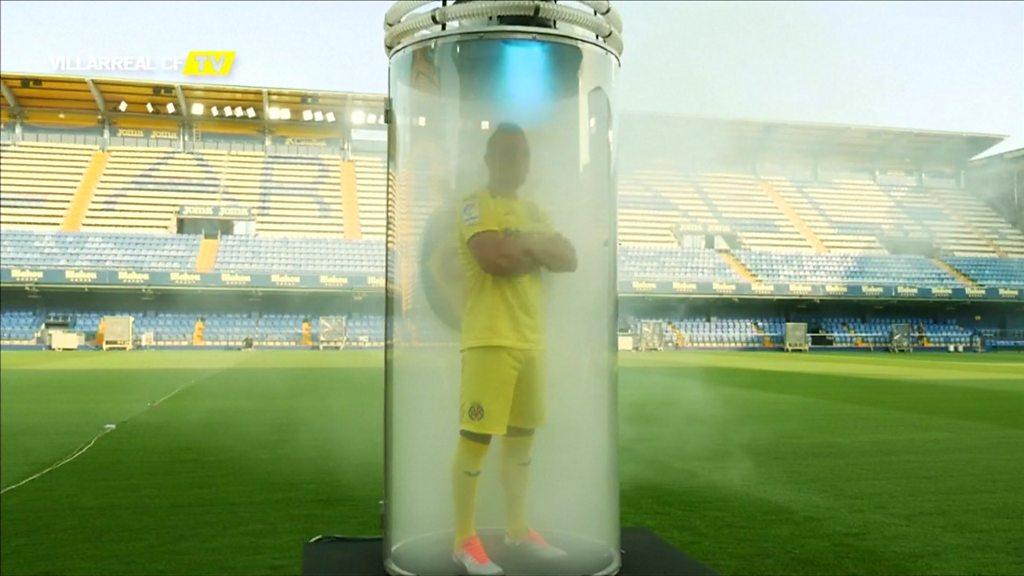 A football player in a glass tube full of smoke on a pitch