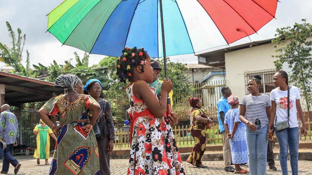 A young girl holds an umbrella in front of a church, in Libreville, Gabon - 10 September 2023