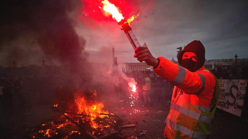 Protester stands with flare by fire during demonstrations in Paris