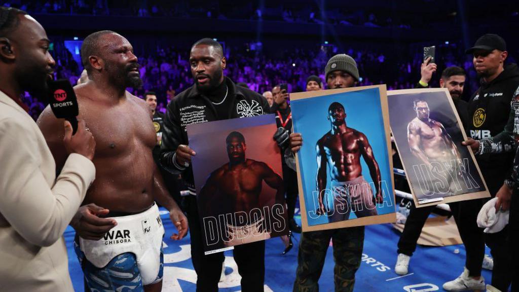 Derek Chisora stands next to pictures of Daniel Dubois, Anthony Joshua and Oleksandr Usyk