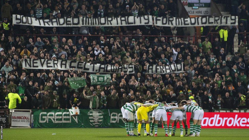 The Celtic players go into their pre match huddle as the Celtic fans unveil a banner aimed at their former manager Brendan Rodgers