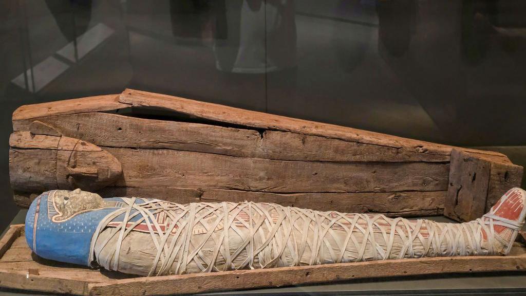 A wooden coffin and mummy, with masks hanging on the wall