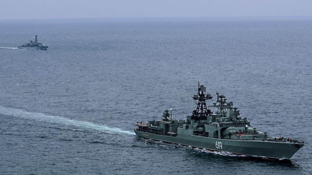 Image shows two ships out at sea. In the foreground is Russian warship RFN Severomorsk 619 and in the top left corner is Royal Navy vessel HMS Somerset
