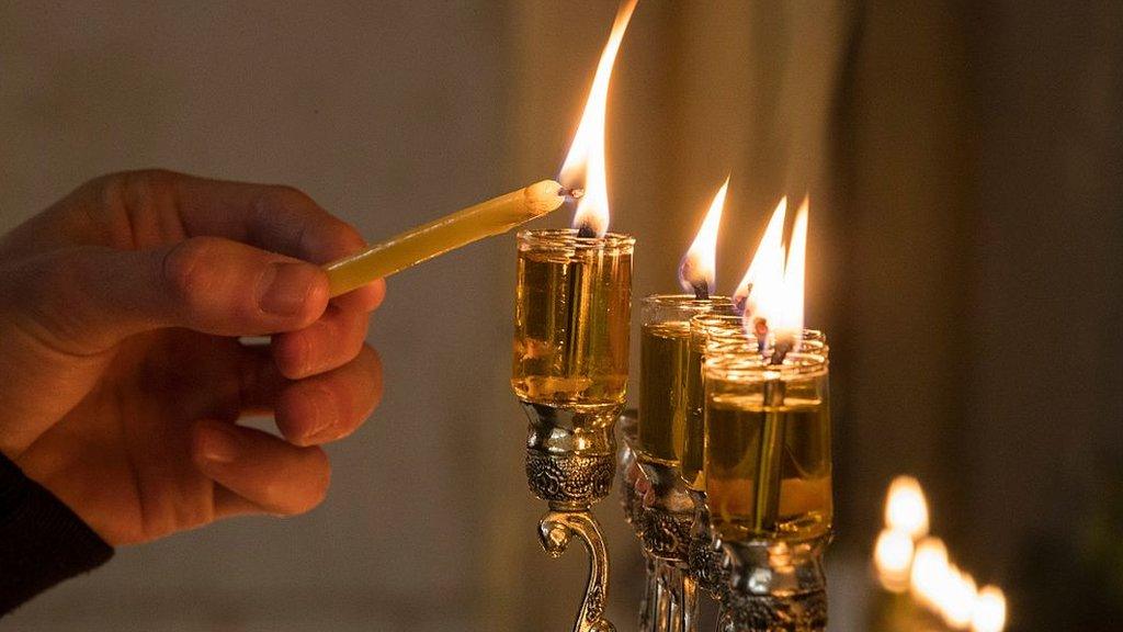 A handle is seen lighting Hanukkah candles