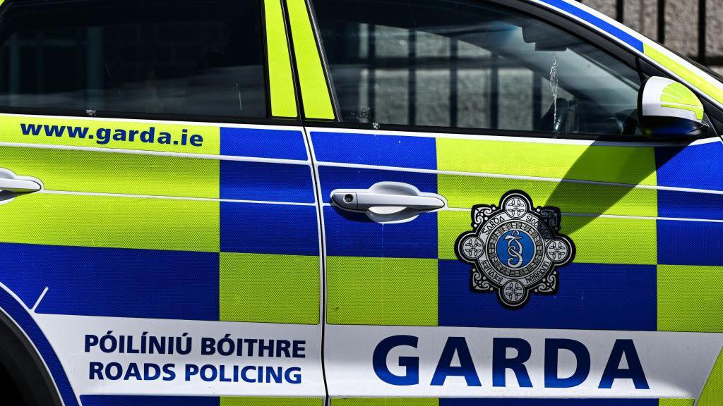 Police car with yellow and blue chequers and the words Garda, Roads Policing and www.garda.ie there is also a garda logo