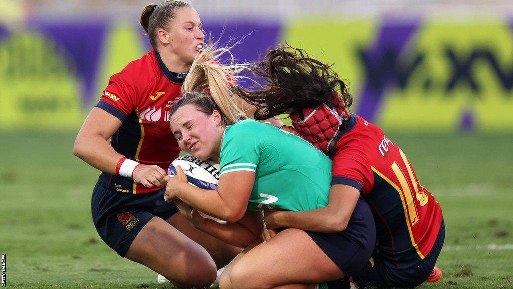 An Ireland player is tackled by two Spain rivals in the WXV3 decider in Dubai