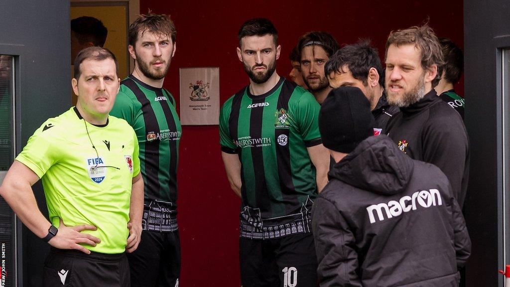 Match officials and Aberystwyth players wait for news at the USW Sport Park in Treforst