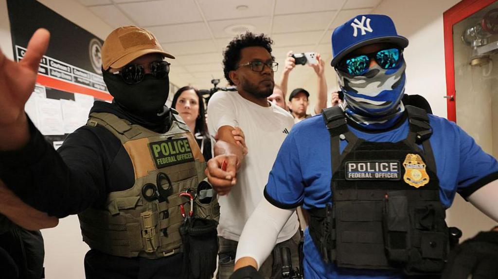 Federal immigration officers wearing masks and sunglasses detain a man who appeared for his hearing at 26 Federal Plaza in New York City on 30 July