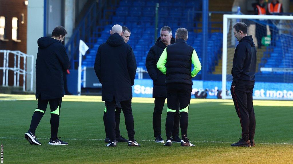 Match officials discuss the pitch with the two managers